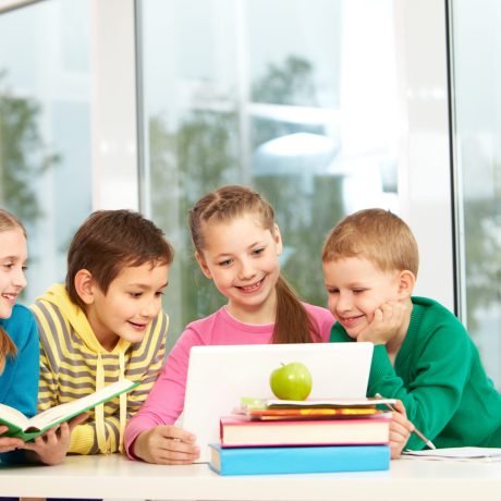 Portrait of smart schoolgirls and schoolboys looking at the laptop in classroom
