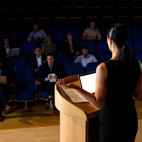 Rear view of female business executive giving a speech at conference center